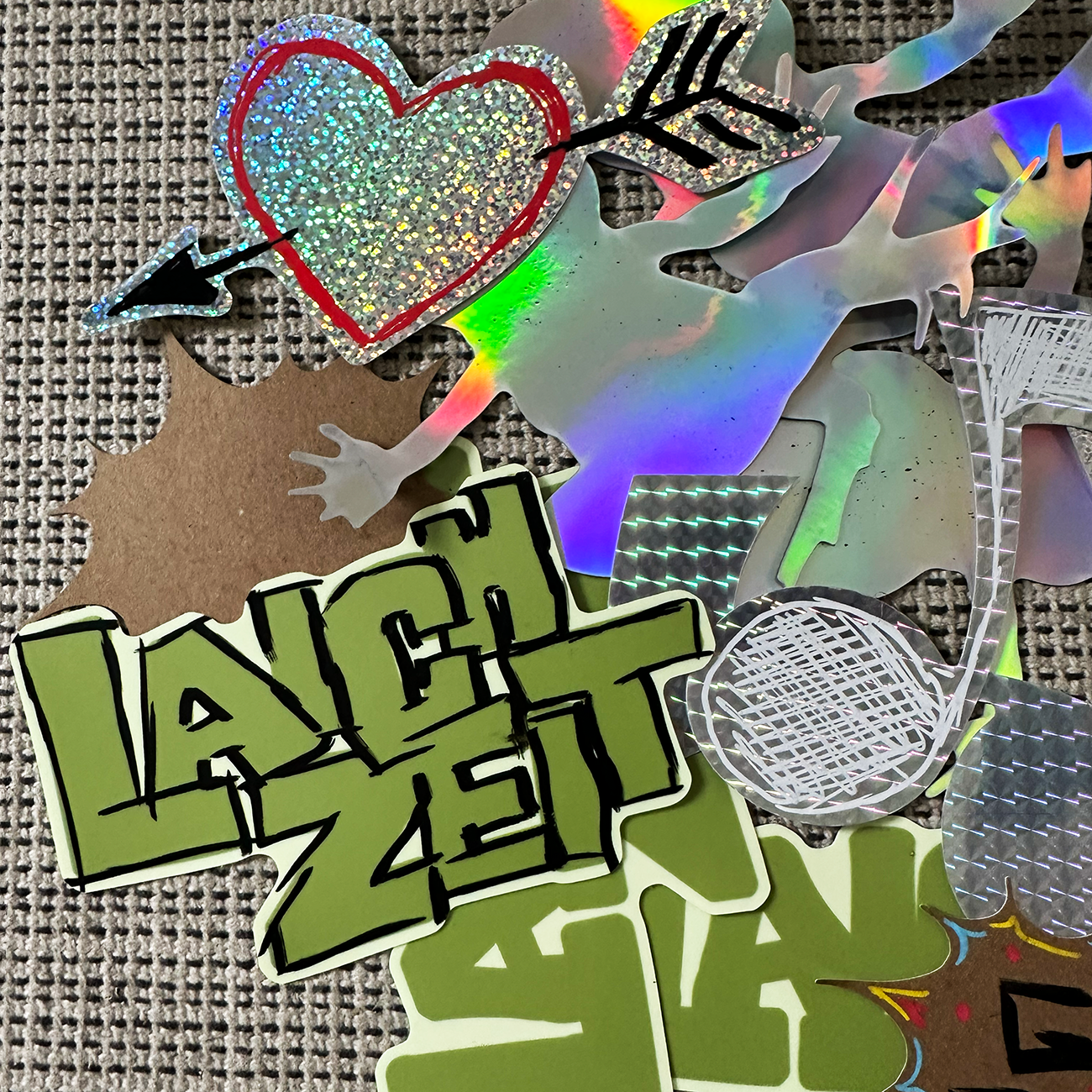 Colorful die-cut stickers with the texk "LAICHZEIT", heart-and note-shaped laying on a beige and black fabric