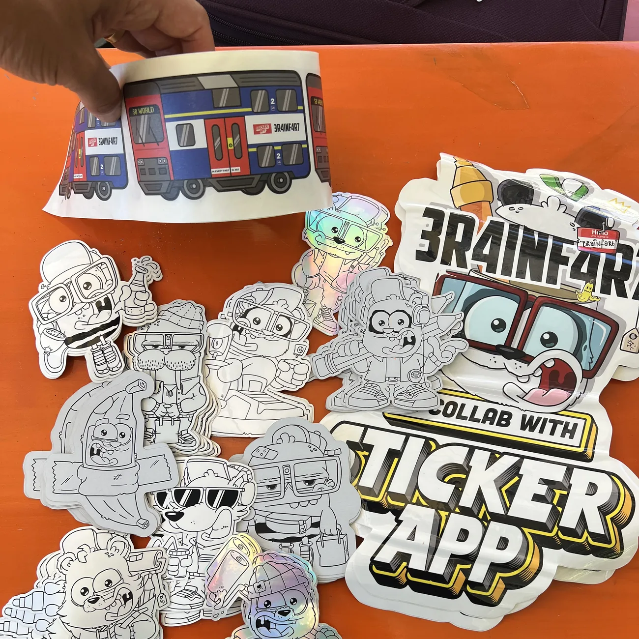 Etikett mit dem S8-World-Zug von Brainfart x StickerApp mit dem Schild "In every fart is art", über schwarz-weißen Freiform-Aufklebern gehalten