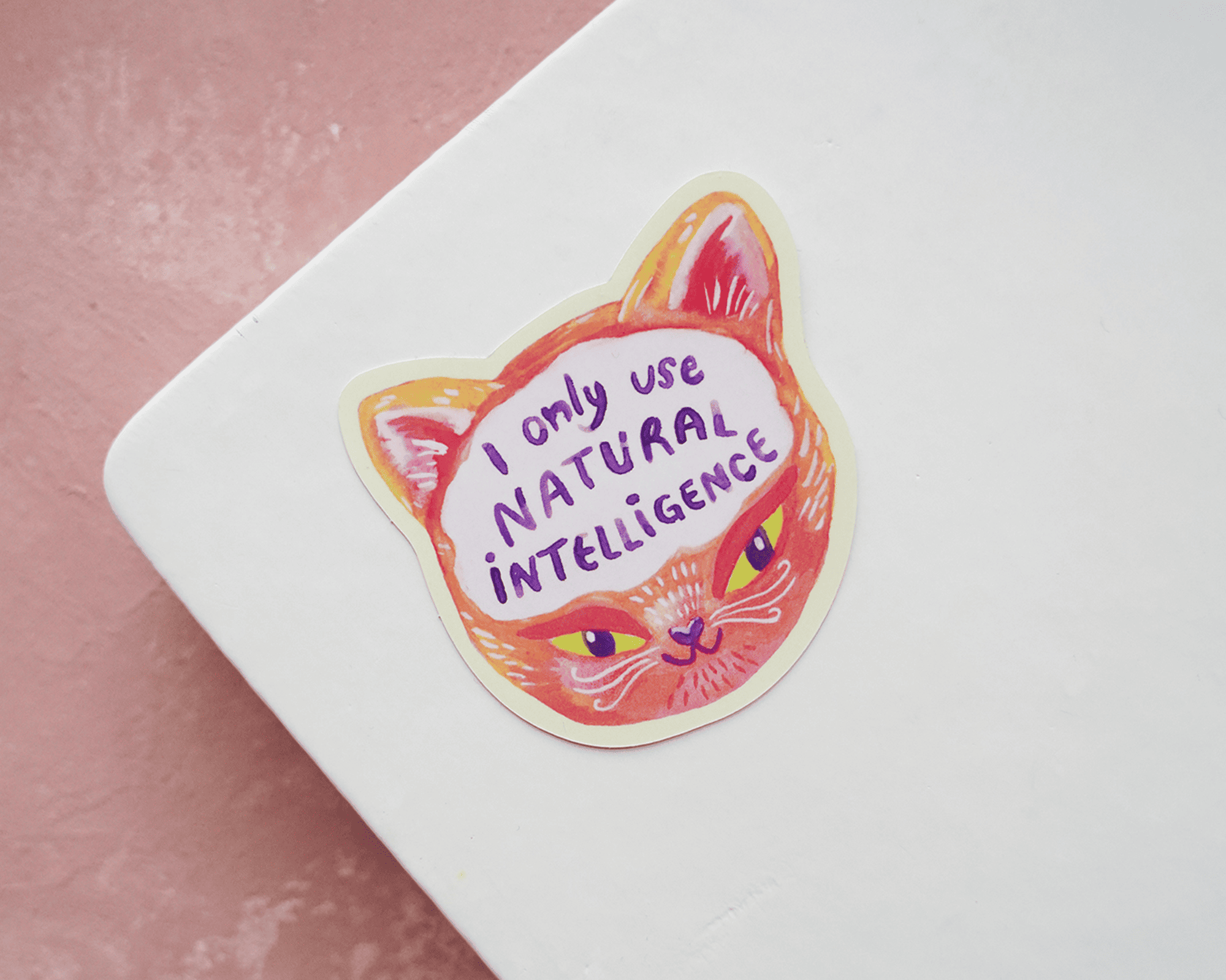 Freiform-Sticker mit Katzengesicht und dem Text "I only use natural intelligence" auf einem weißen Notizbuch